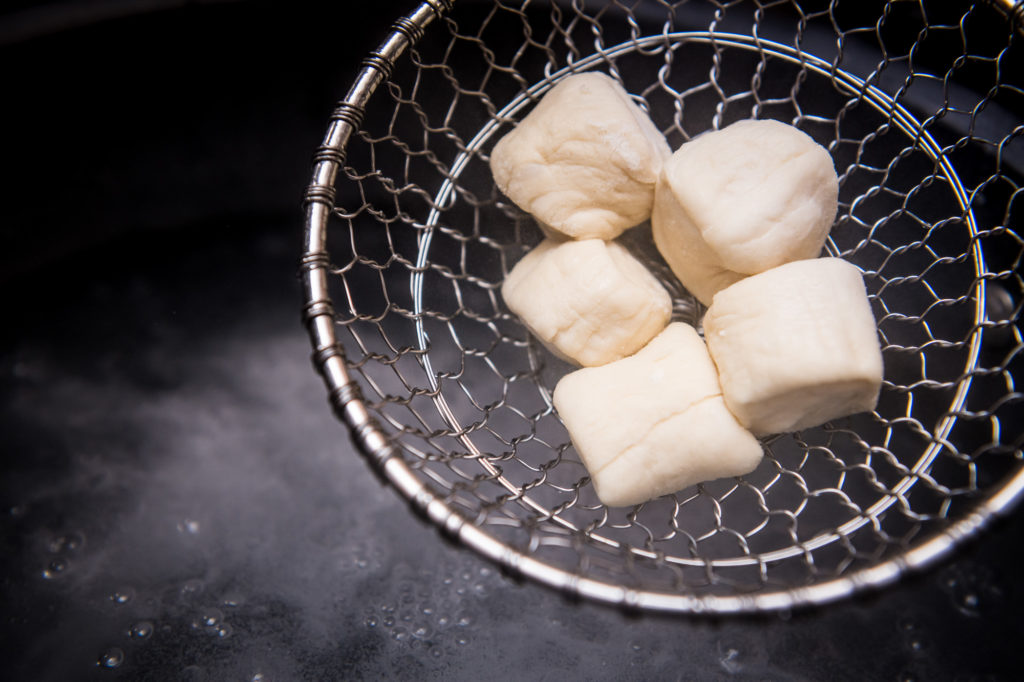 Unbaked vegan pretzel bites in spider over boiling water