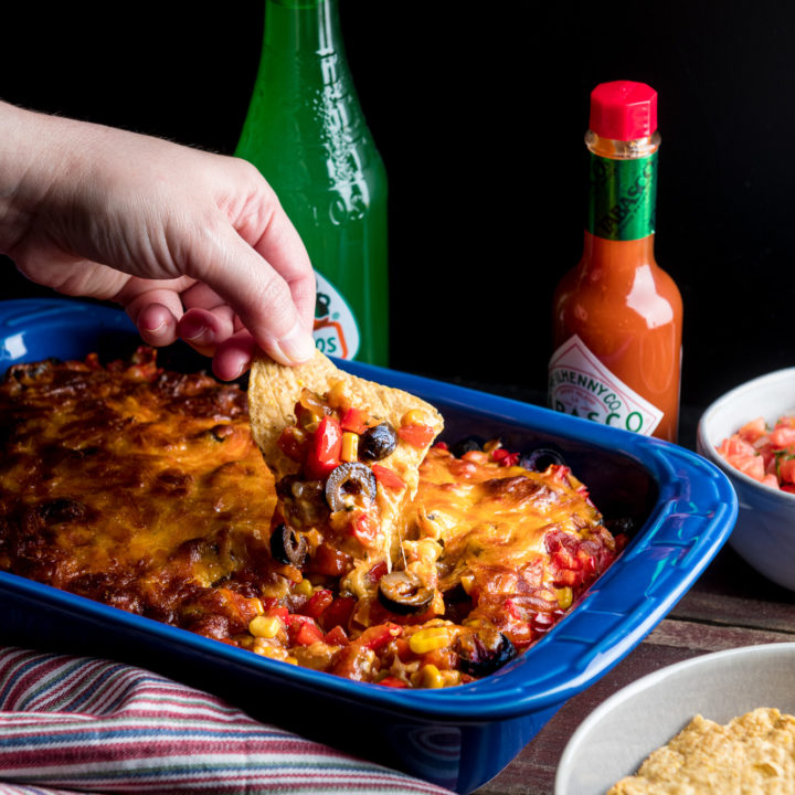Hand dipping into baked taco dip