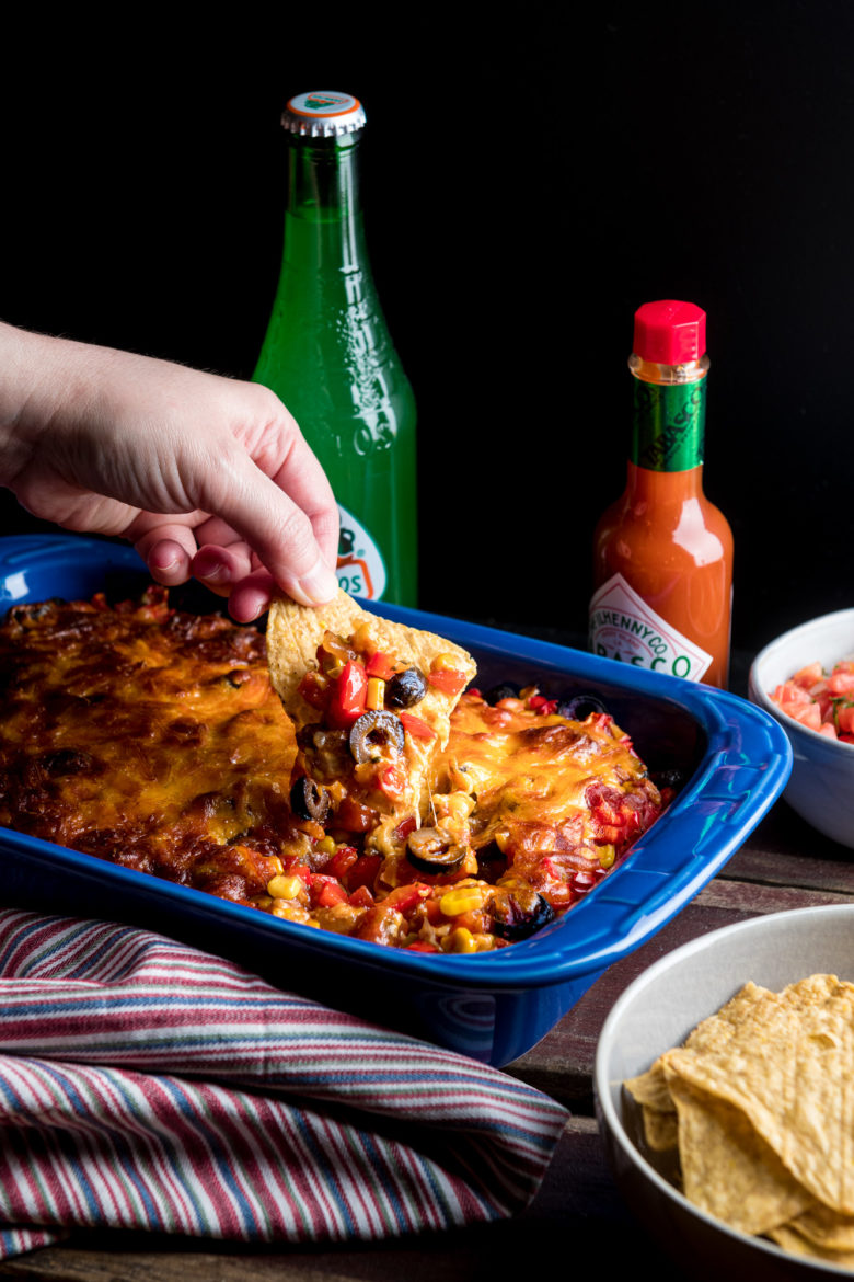 Hand dipping into baked taco dip